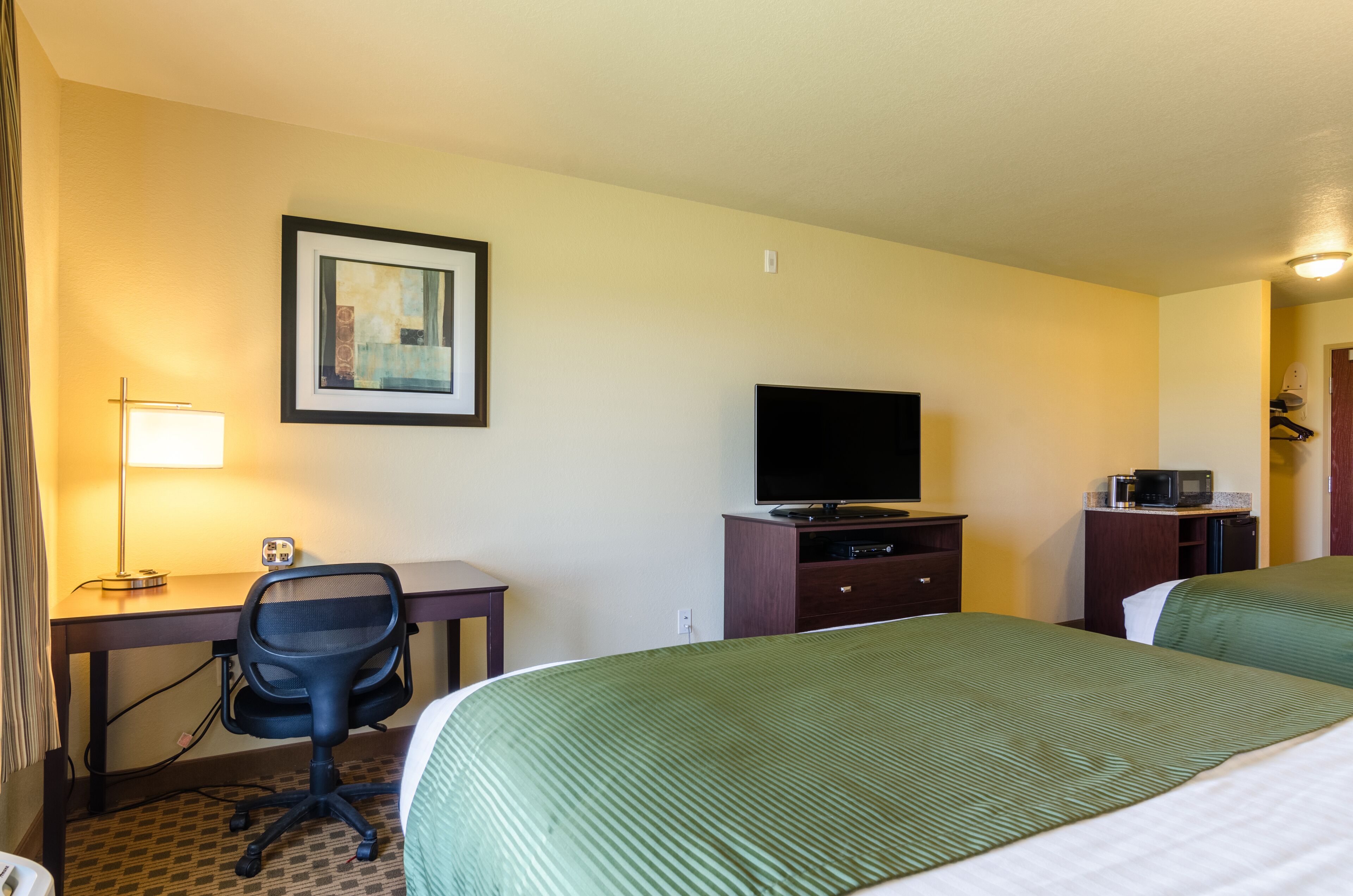 Une chambre d’hôtel avec deux lits, un bureau avec une chaise, une télévision, un four à micro-ondes et un tableau encadré au mur.