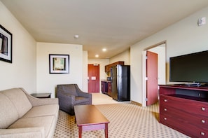 Cozy living space with a kitchenette, sofa, and armchair, featuring a flat-screen TV and a small dining table.