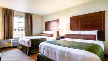 Habitación de hotel con dos camas, un ventanal grande con cortinas, cabecero de madera, mesita de noche con lámpara y alfombra estampada.