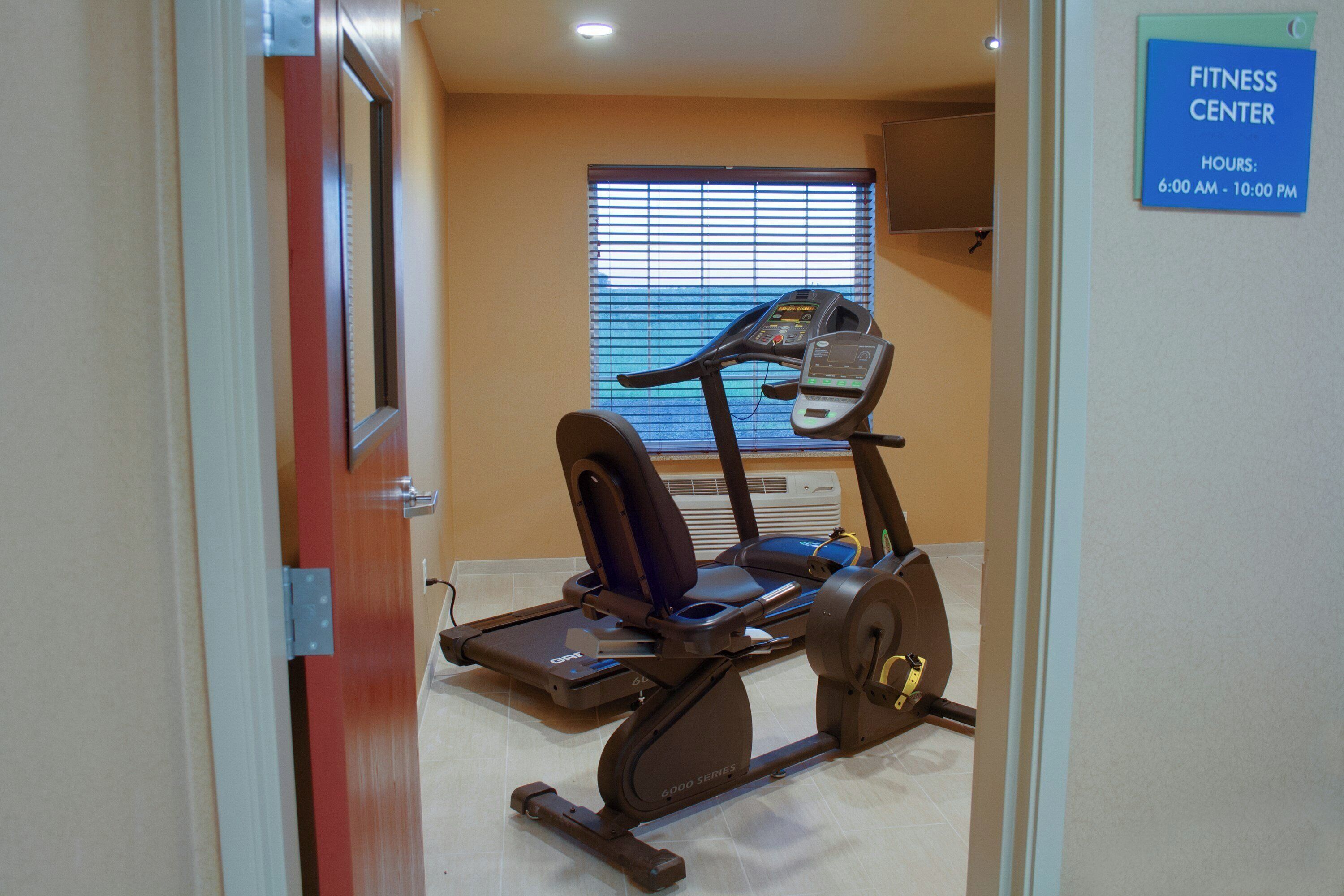 Un centre de remise en forme équipé d’un vélo d’exercice, d’un tapis de course et d’un panneau indiquant les heures d’ouverture.