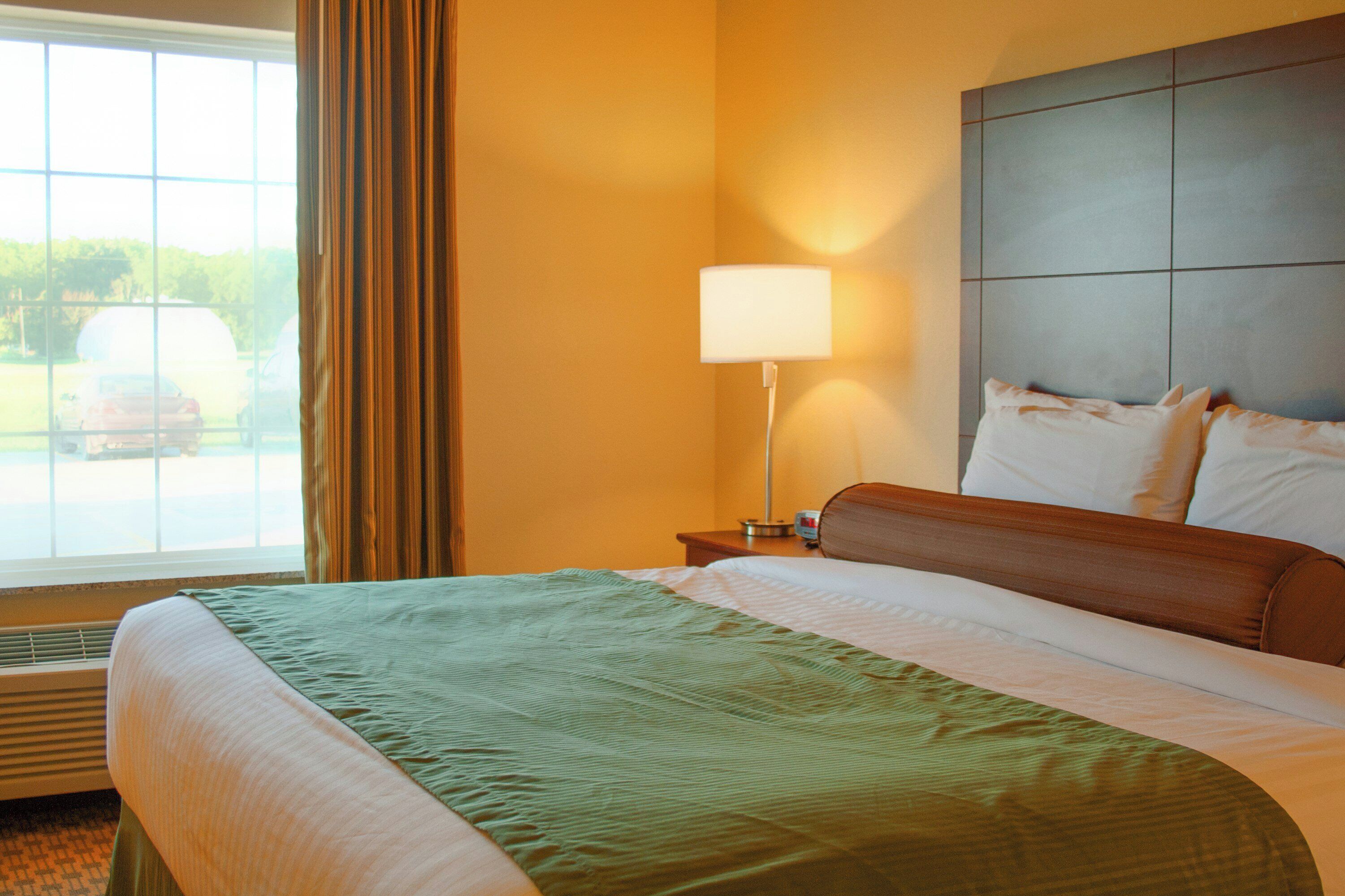A hotel room with a bed, a nightstand, a lamp, and a window with curtains.