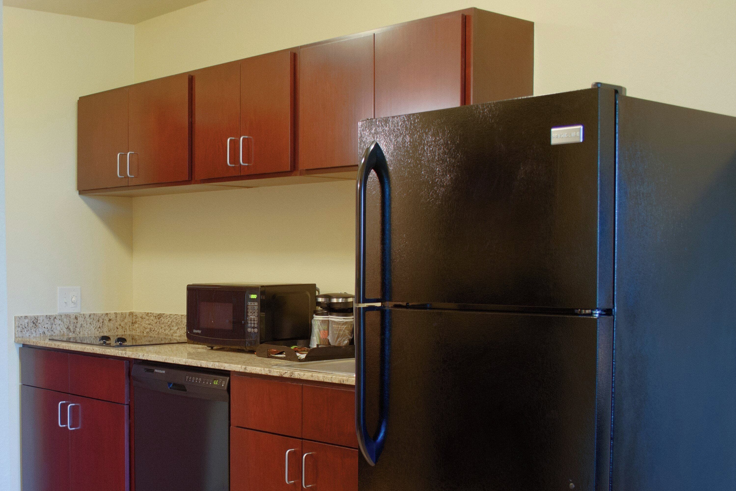 A kitchen with a black refrigerator, wooden cabinets, a microwave, and a dishwasher.