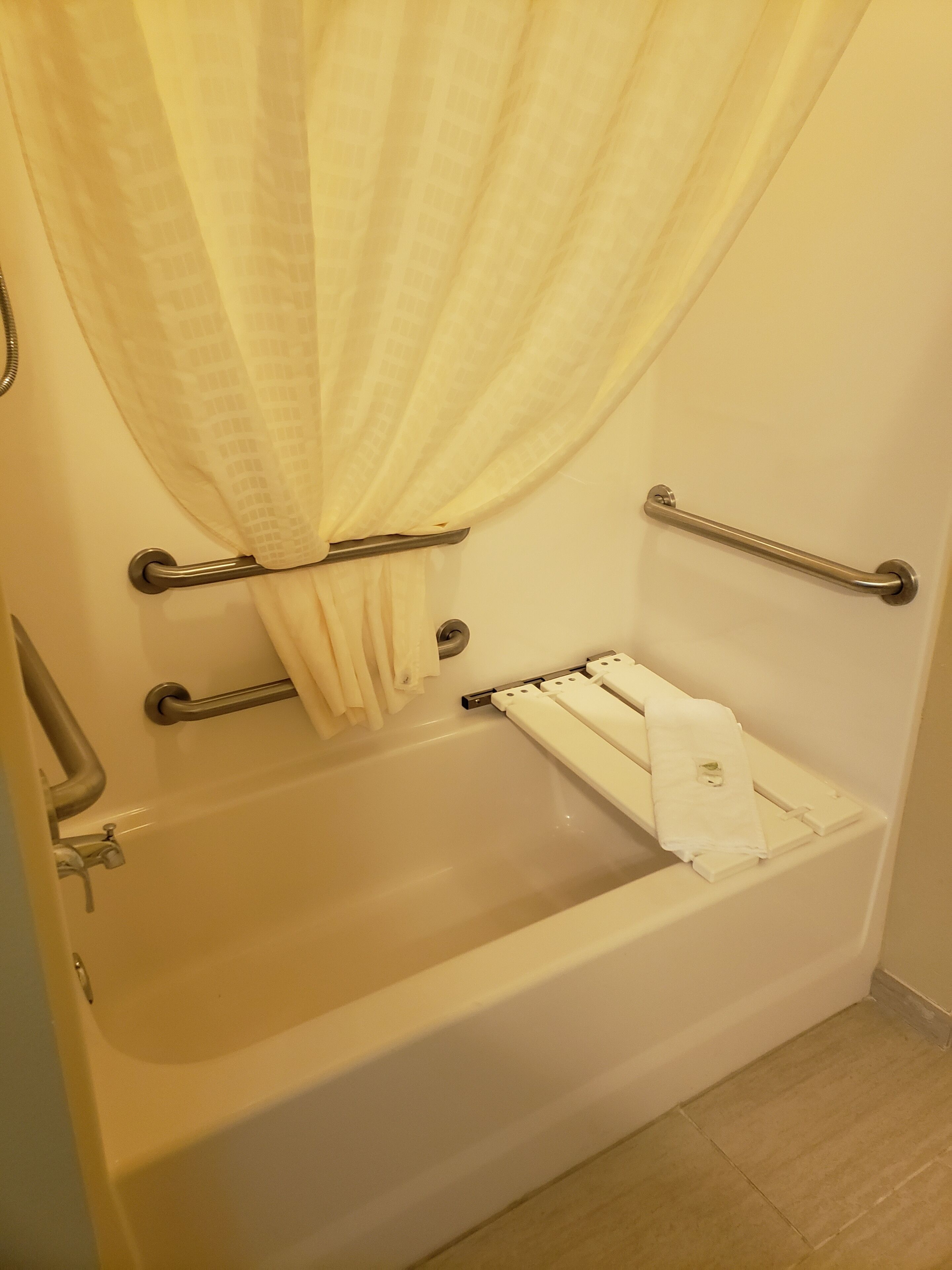 Una bañera con barras de apoyo, un perchero y una cortina de ducha.