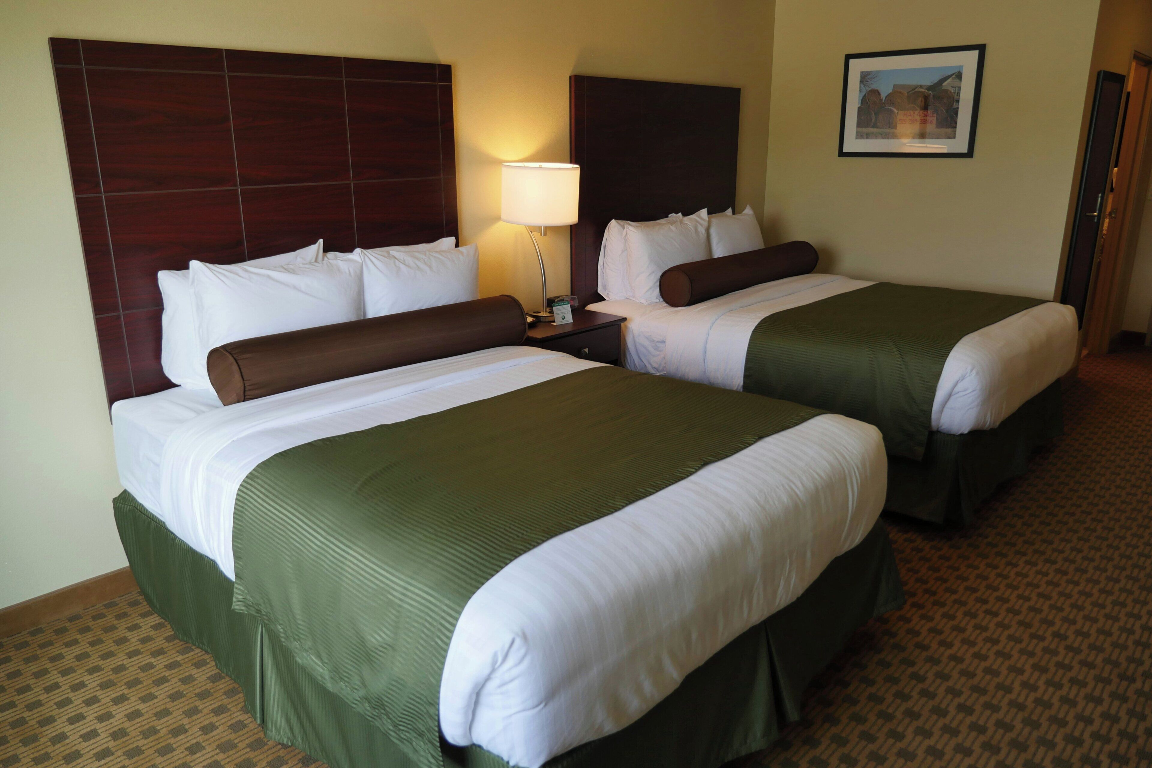A hotel room with two beds, a nightstand, a lamp, and a framed picture on the wall.