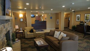 A hotel lobby with a reception desk, a brown sofa, a small armchair, a coffee table, and a fireplace. - Cobblestone Inn & Suites - Winterset, IA (Winterset)