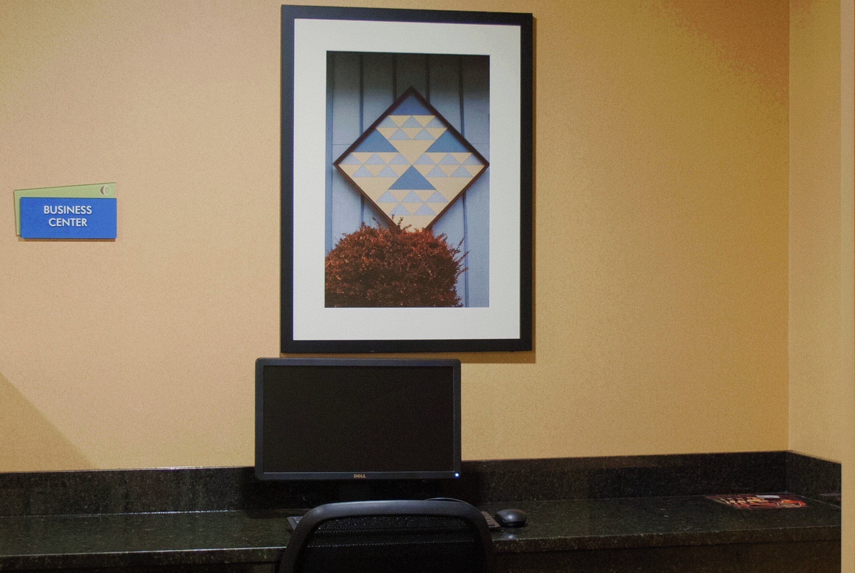A business center with a framed geometric artwork, a Dell laptop, and a sign indicating the business center location.