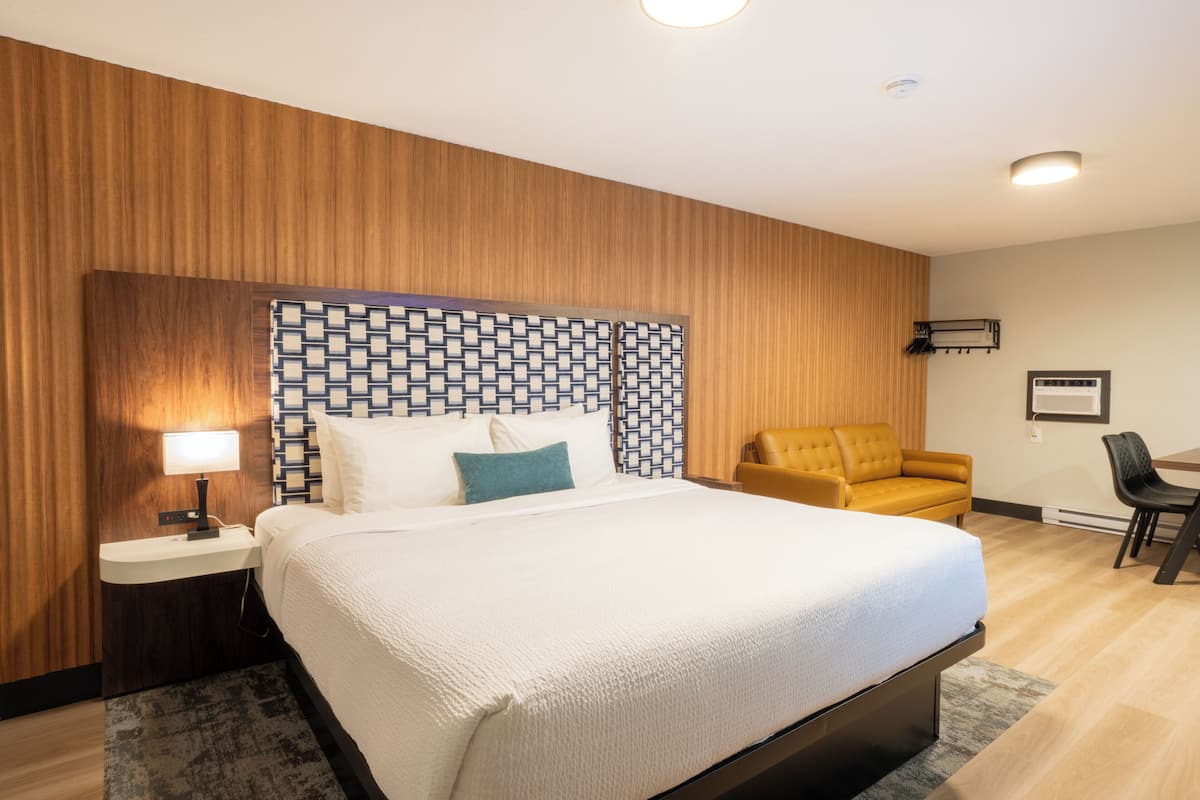 A hotel room with a bed, bedside table, lamp, and a patterned headboard.
