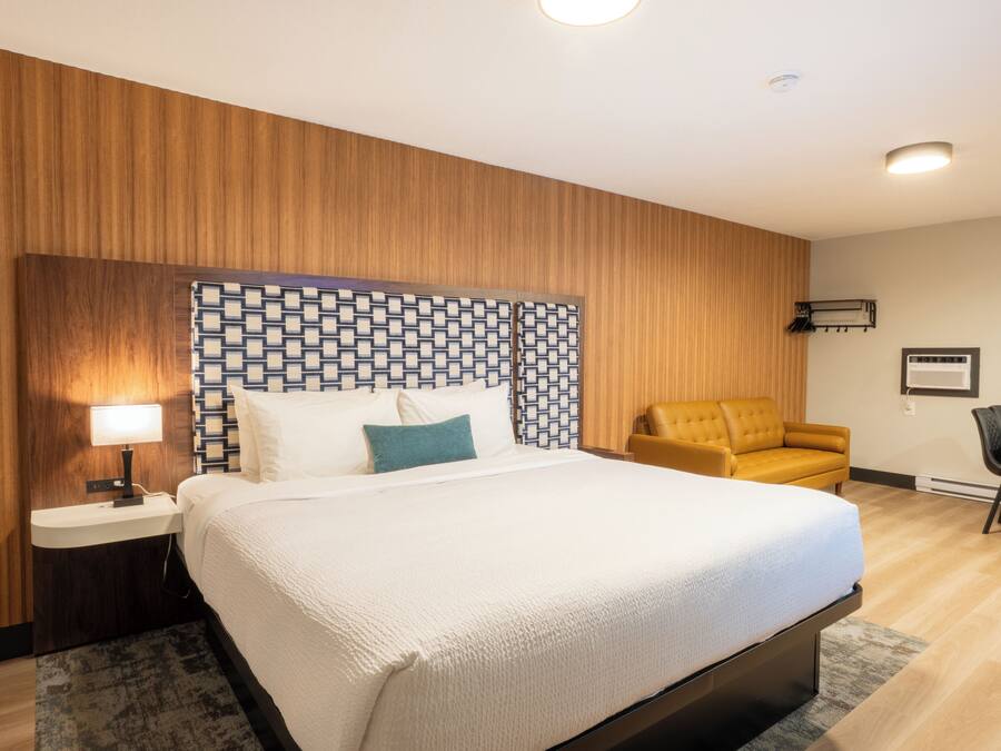 A hotel room with a bed, bedside table, lamp, and a patterned headboard.