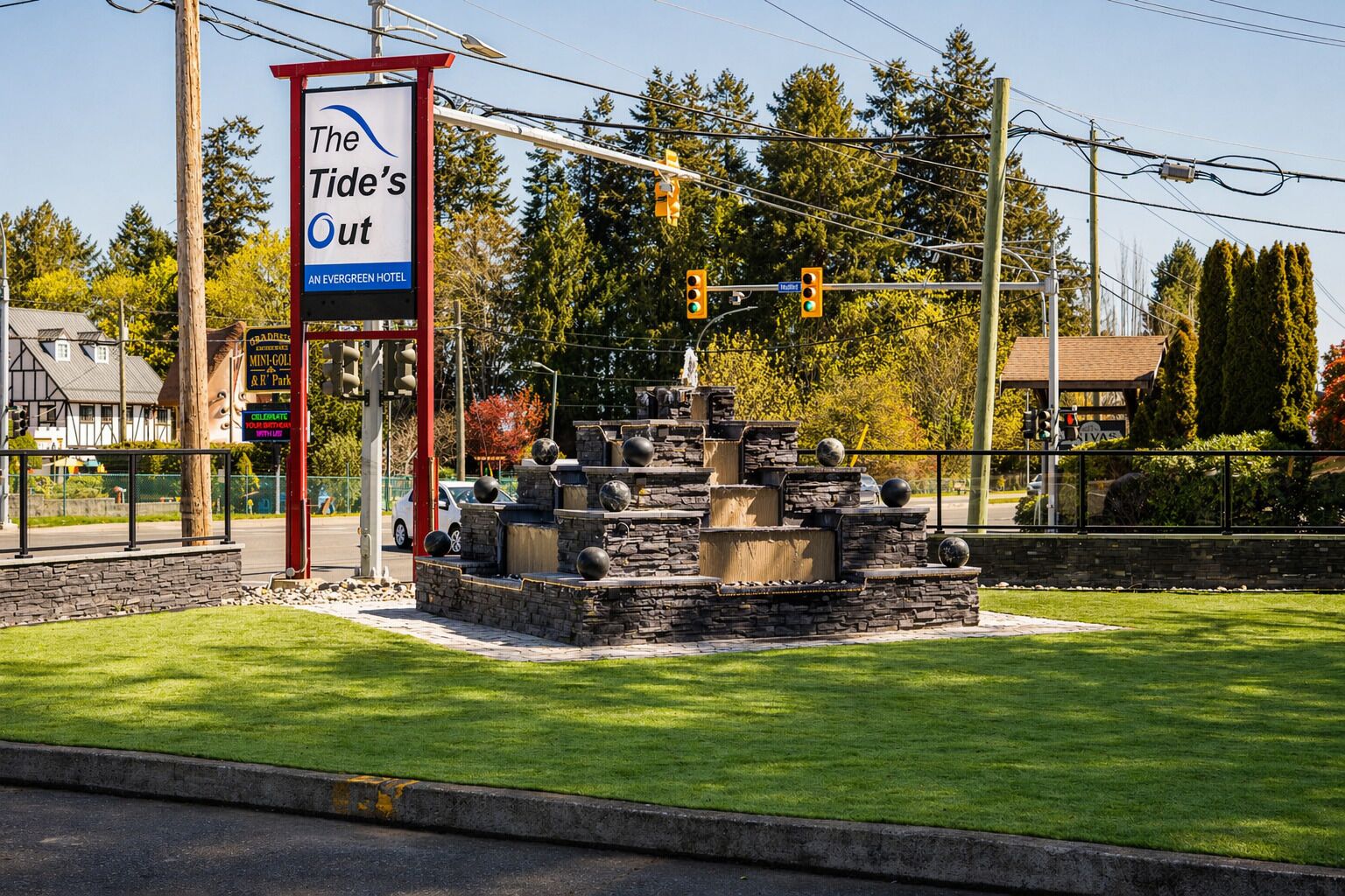 A landscaped area with a stone fountain, a sign for 'The Tide's Out' hotel, and a traffic light.