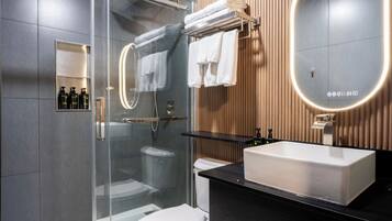 A modern bathroom with a glass shower enclosure, a white toilet, a black countertop, a large mirror, and a wooden wall panel.