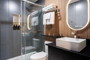A modern bathroom with a glass shower enclosure, a white toilet, a black countertop, a large mirror, and a wooden wall panel.
