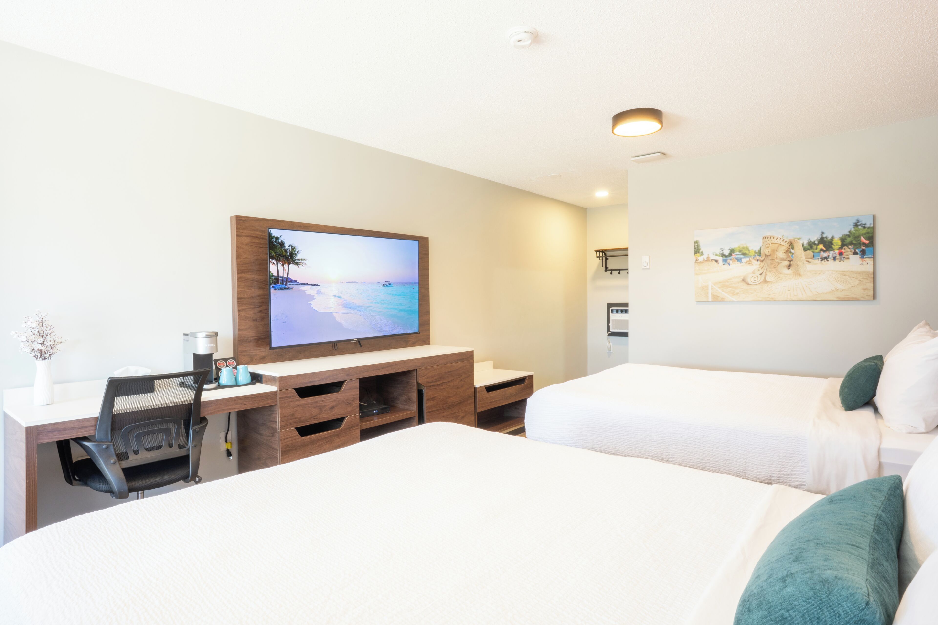 A hotel room with a bed, a desk with a computer, a television, and a painting on the wall.