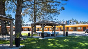 A gazebo with seating, a paved walkway, and a building with orange windows in the background. - The Tide’s Out (Parksville)
