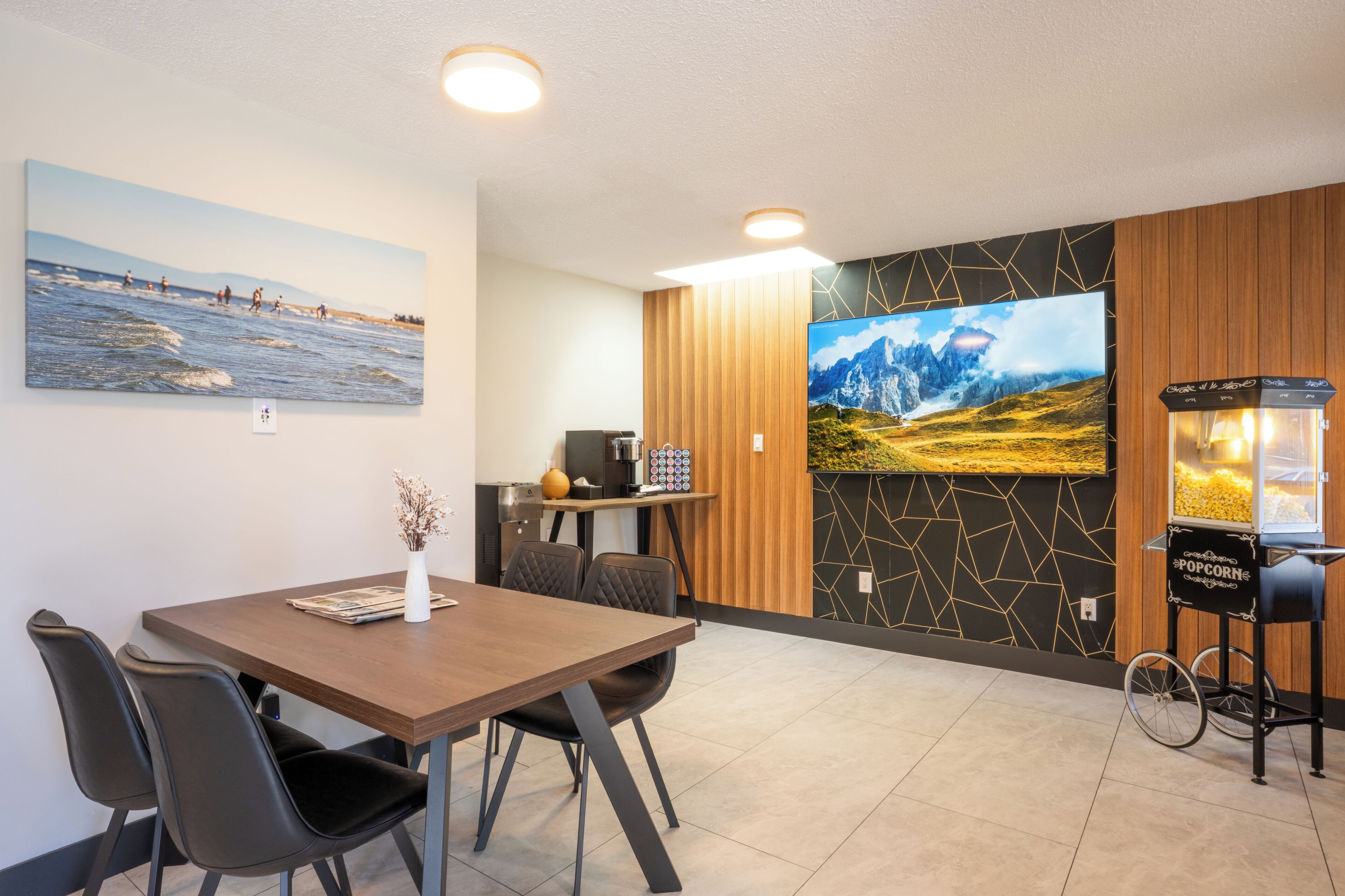 A modern dining area with a wooden table, black chairs, a small vase, and a wall-mounted TV.