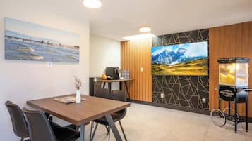 A modern dining area with a wooden table, black chairs, a small vase, and a wall-mounted TV.