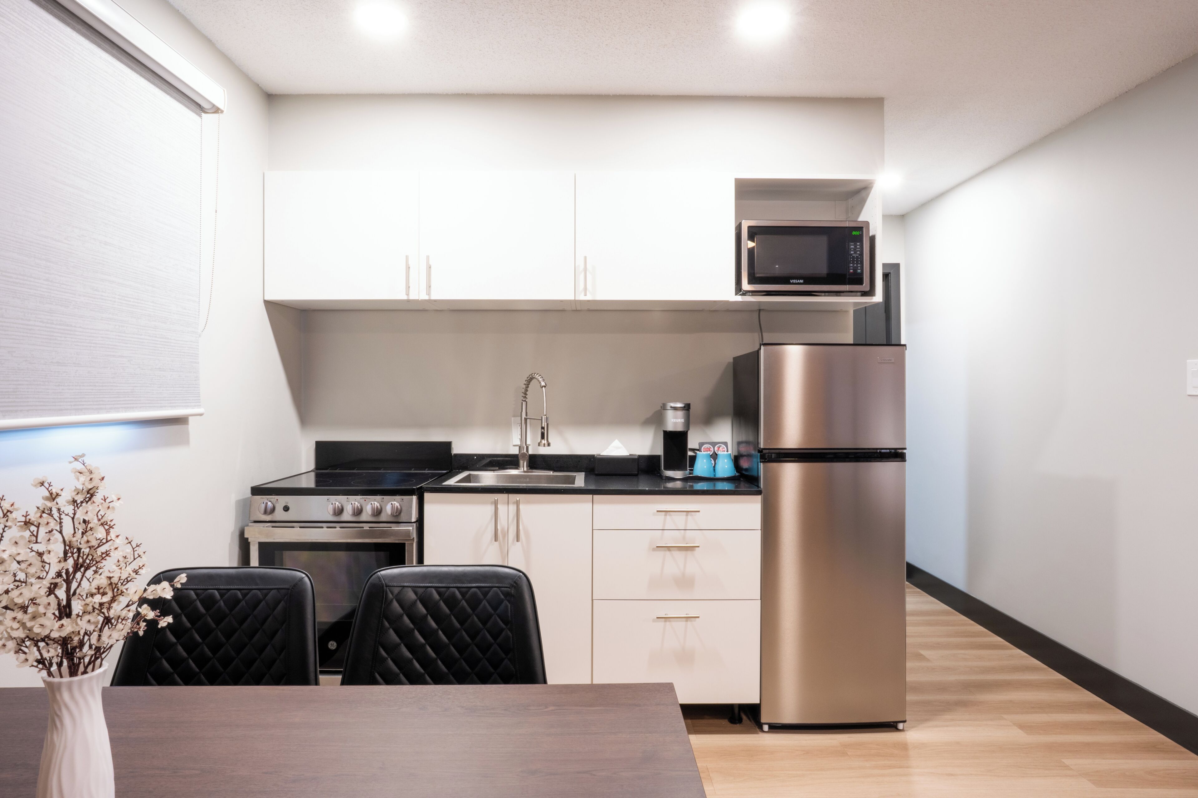A modern kitchen with stainless steel appliances, a dining area with a table and chairs, and a vase with flowers.