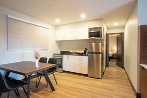 A compact kitchen with modern appliances, a dining area with a table and chairs, and a hallway leading to a bedroom.