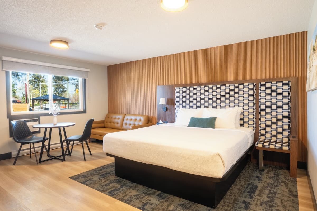 A hotel room with a large bed, a sofa, a small table, and a chair.
