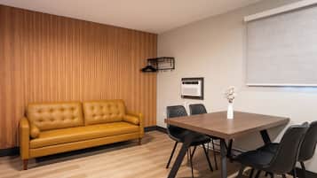 Una habitación moderna con un panel de madera en la pared, un sofá amarillo, una mesa de comedor de madera con cuatro sillas y una ventana con persianas.