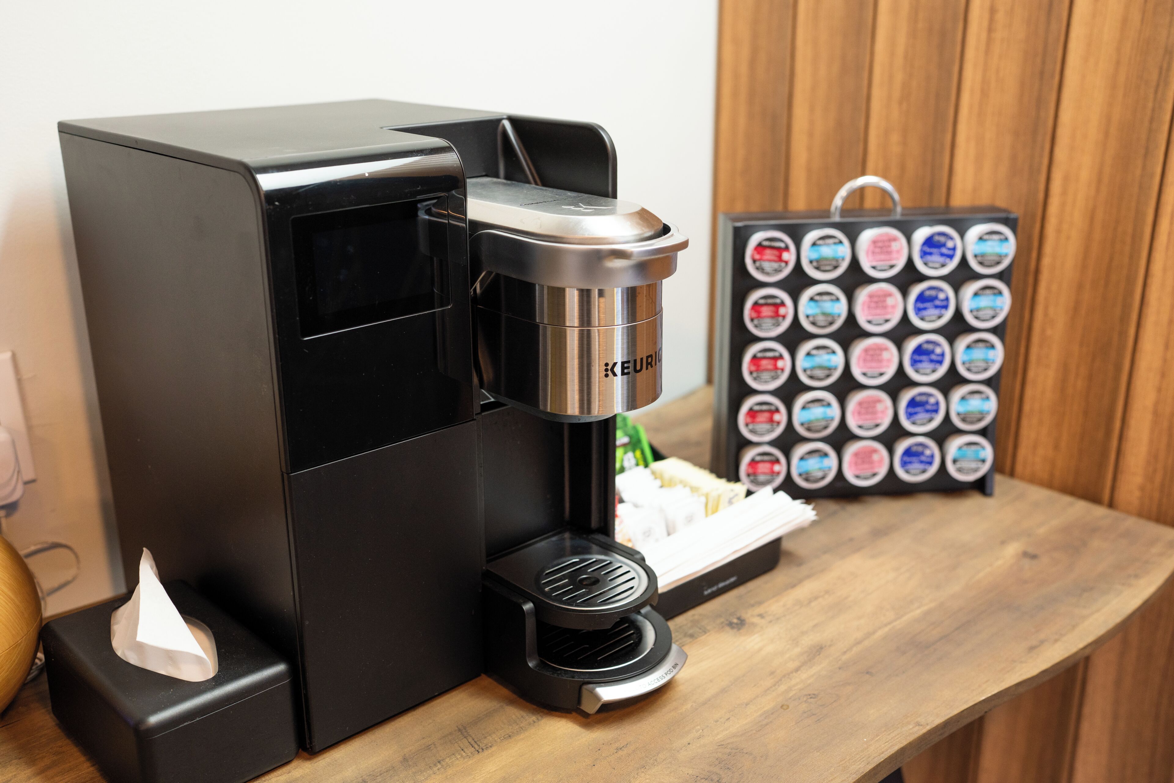 A Keurig coffee machine with a coffee pod holder and a tissue box on a wooden table.