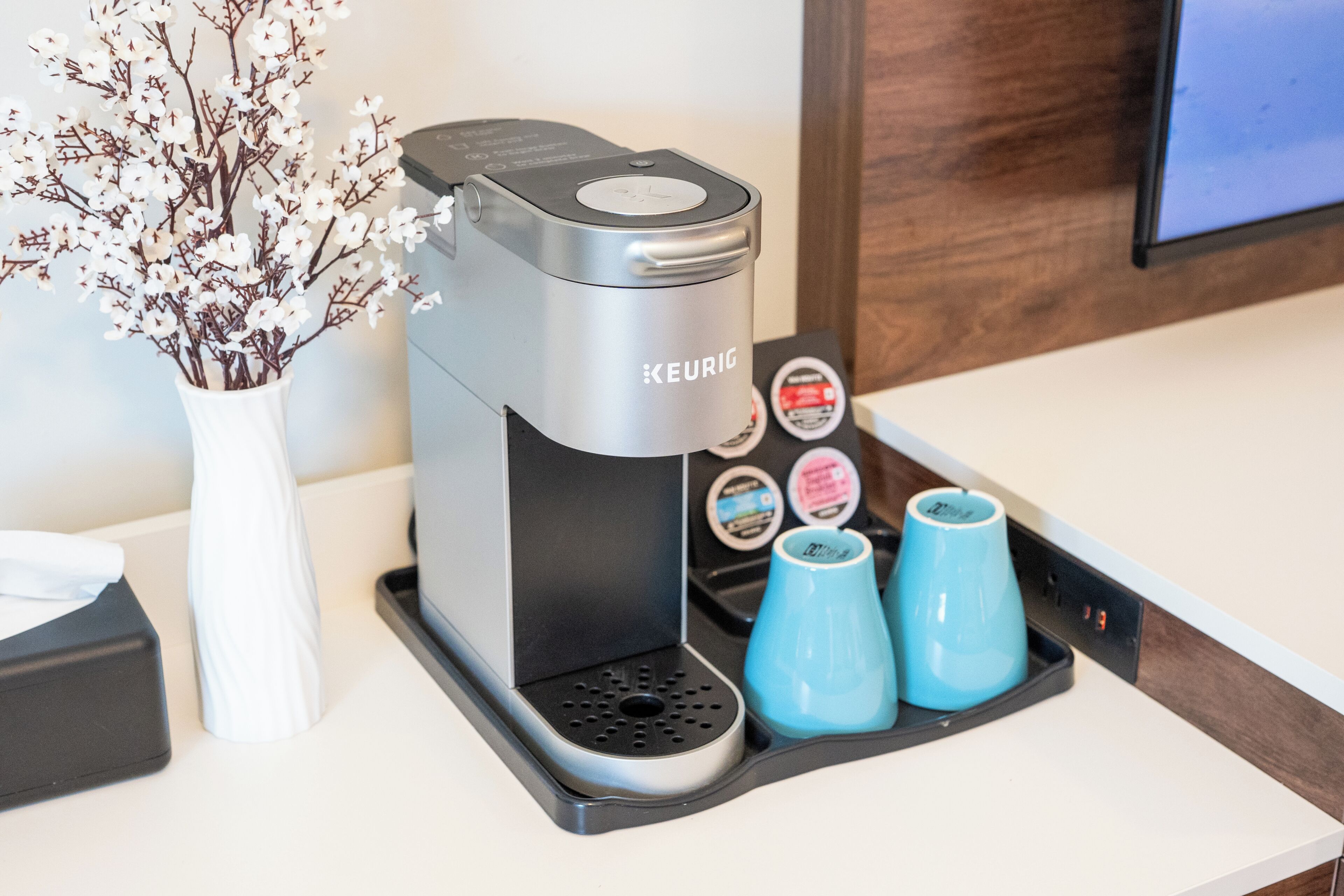 A Keurig coffee maker with a coffee pod holder and two blue mugs on a countertop.