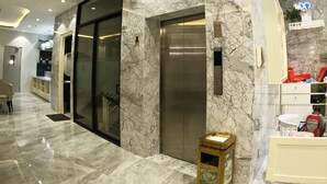 Un moderno ascensor con paredes de mármol y un diseño elegante, un pasillo bien iluminado con suelo de mármol, y una pequeña caja de madera en el suelo.