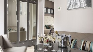 A modern living room with a glass coffee table, several champagne glasses, and a bottle of champagne. There is a beige sofa and a large mirror reflecting the room.