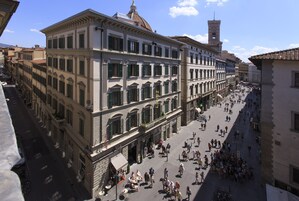 Un edificio storico con diversi piani, ampie finestre e un cortile centrale con persone e posti a sedere all'aperto.