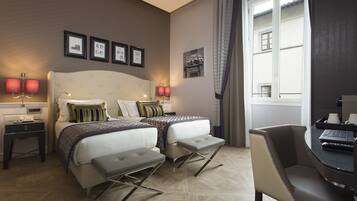 Habitación de hotel con dos camas, un escritorio y una silla. En la pared hay cuadros enmarcados y una ventana con cortinas.