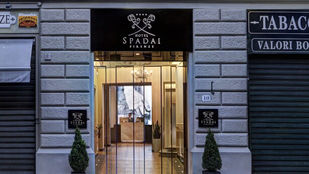 The entrance to Hotel Spadaï Firenze with a modern design, including a reception desk and a chandelier.