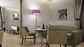 A modern hotel room with a sofa, two armchairs, a small round table with a lamp, and a painting on the wall.