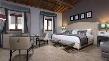 A hotel room with a bed, a chair, a small table, and a desk with a lamp.