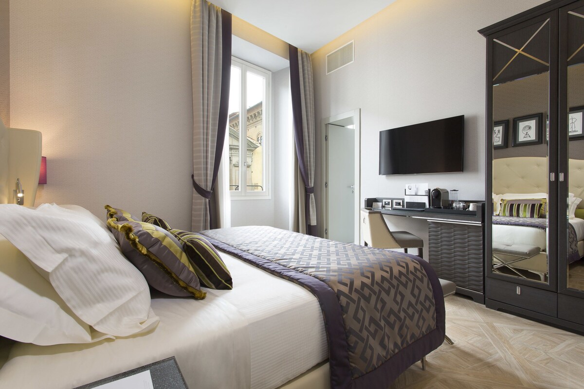 A hotel room with a bed, a desk, a television, and a wardrobe.