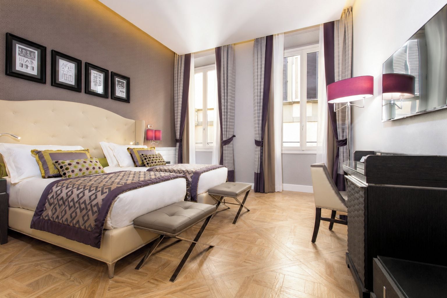 A hotel room with two beds, a desk, and a TV.