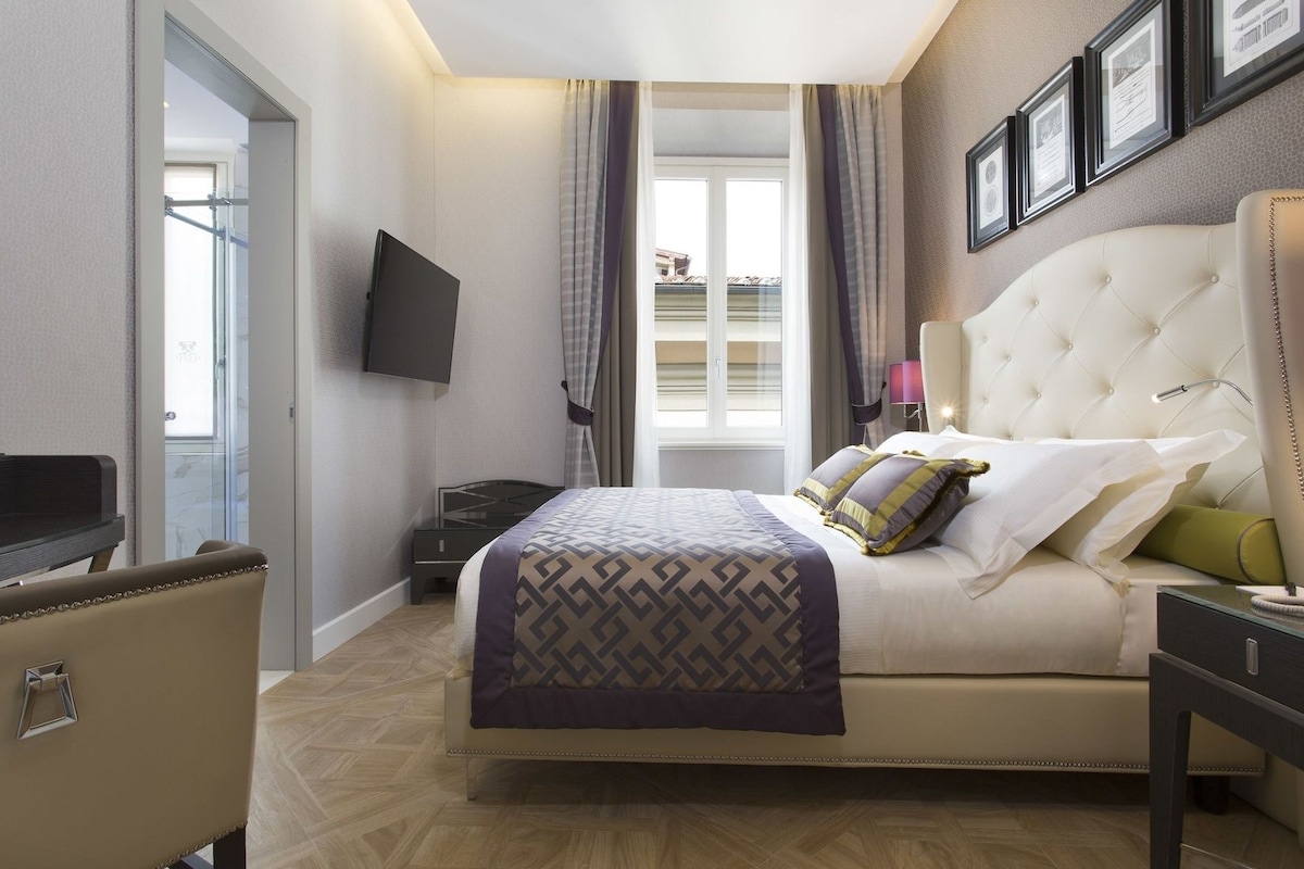 Habitación de hotel con cama, televisor, escritorio y ventana con cortinas.