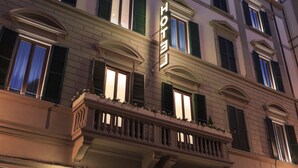 A hotel facade with multiple windows, green shutters, and a balcony with railings.