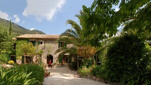 A stone building with a tiled roof, surrounded by lush greenery and a mountain backdrop. -  Sa Vall Turismo de Interior (Valldemossa)
