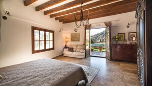 A bedroom with a large bed, a sofa, and a view of a garden through an open door. -  Sa Vall Turismo de Interior (Valldemossa)