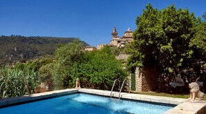 A swimming pool with a stone border, surrounded by lush greenery and a view of a hillside with buildings. -  Sa Vall Turismo de Interior (Valldemossa)