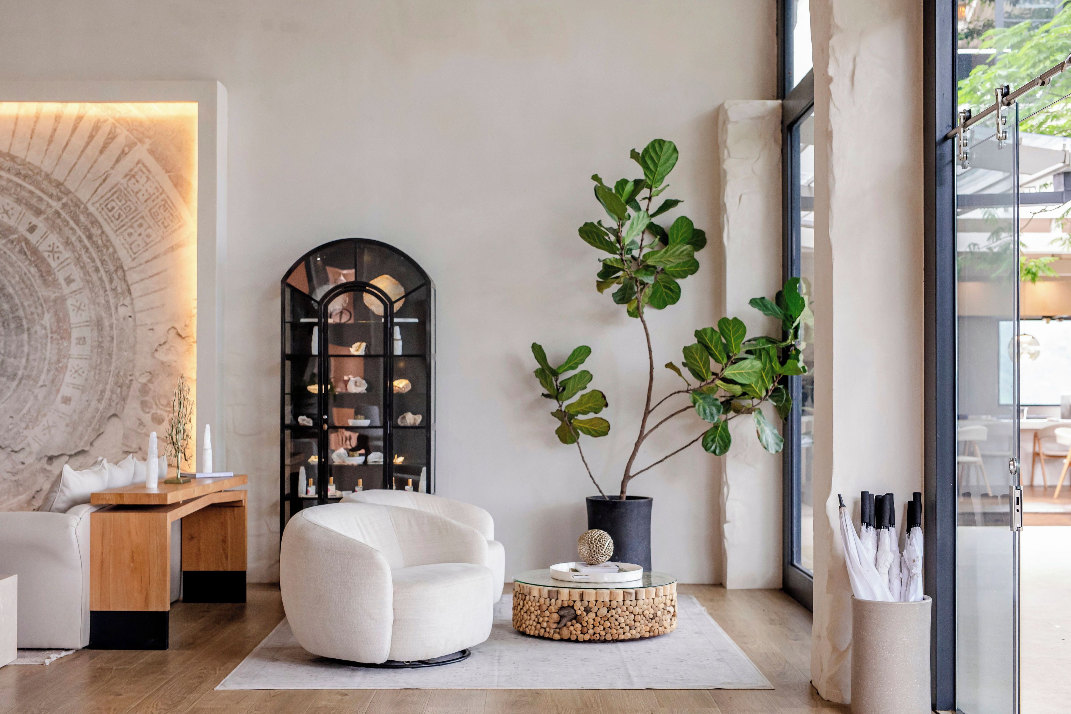 Una sala de estar moderna con un sofá blanco, una mesita redonda de madera, una planta en maceta y una estantería negra de arco.