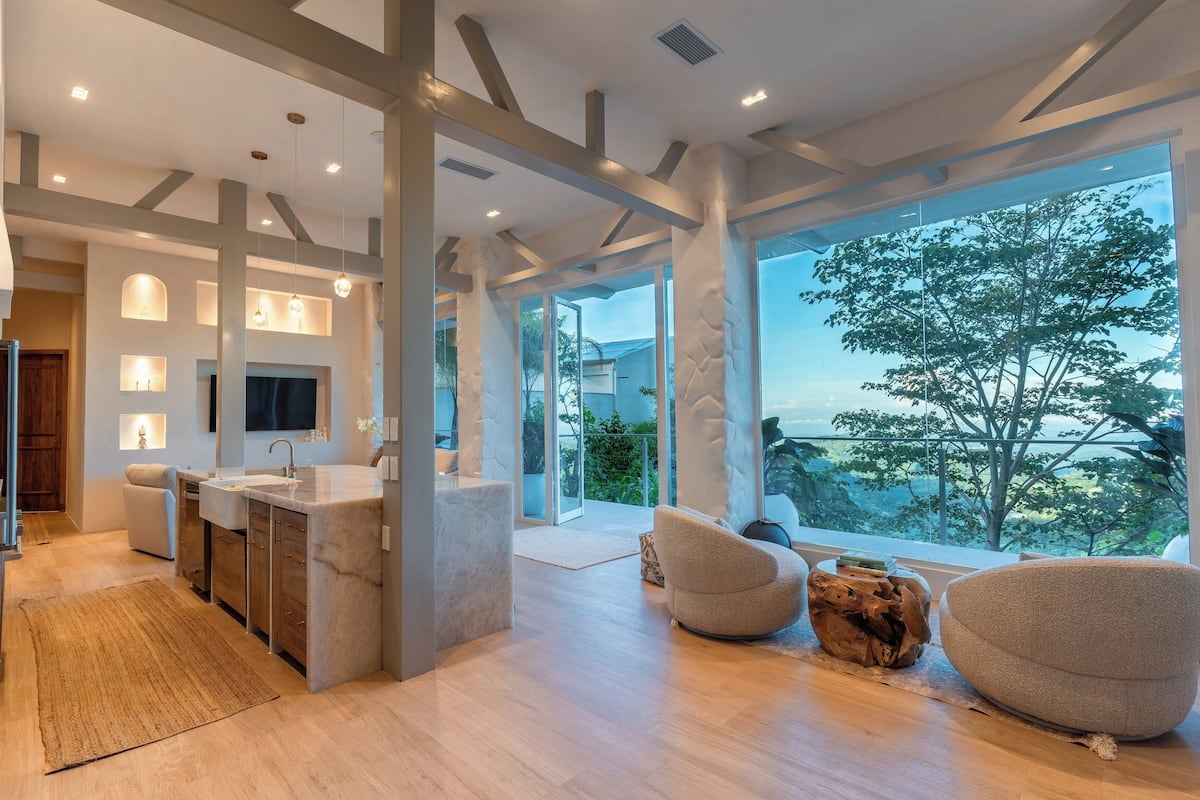 A modern kitchen with a central island, a large window with a view, and a cozy seating area with a unique wooden coffee table.