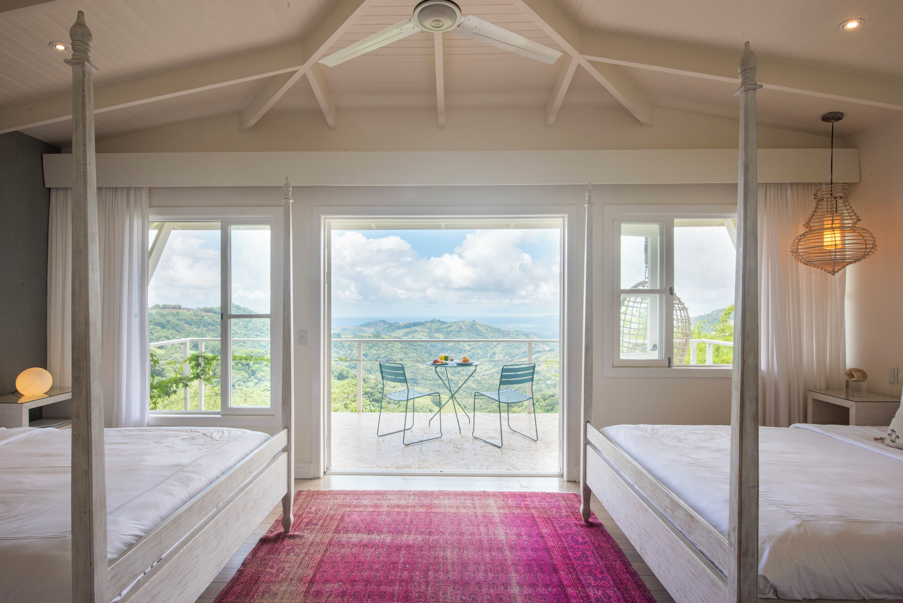 A bedroom with a four-poster bed, a balcony with a table and chairs, and a view of the mountains.