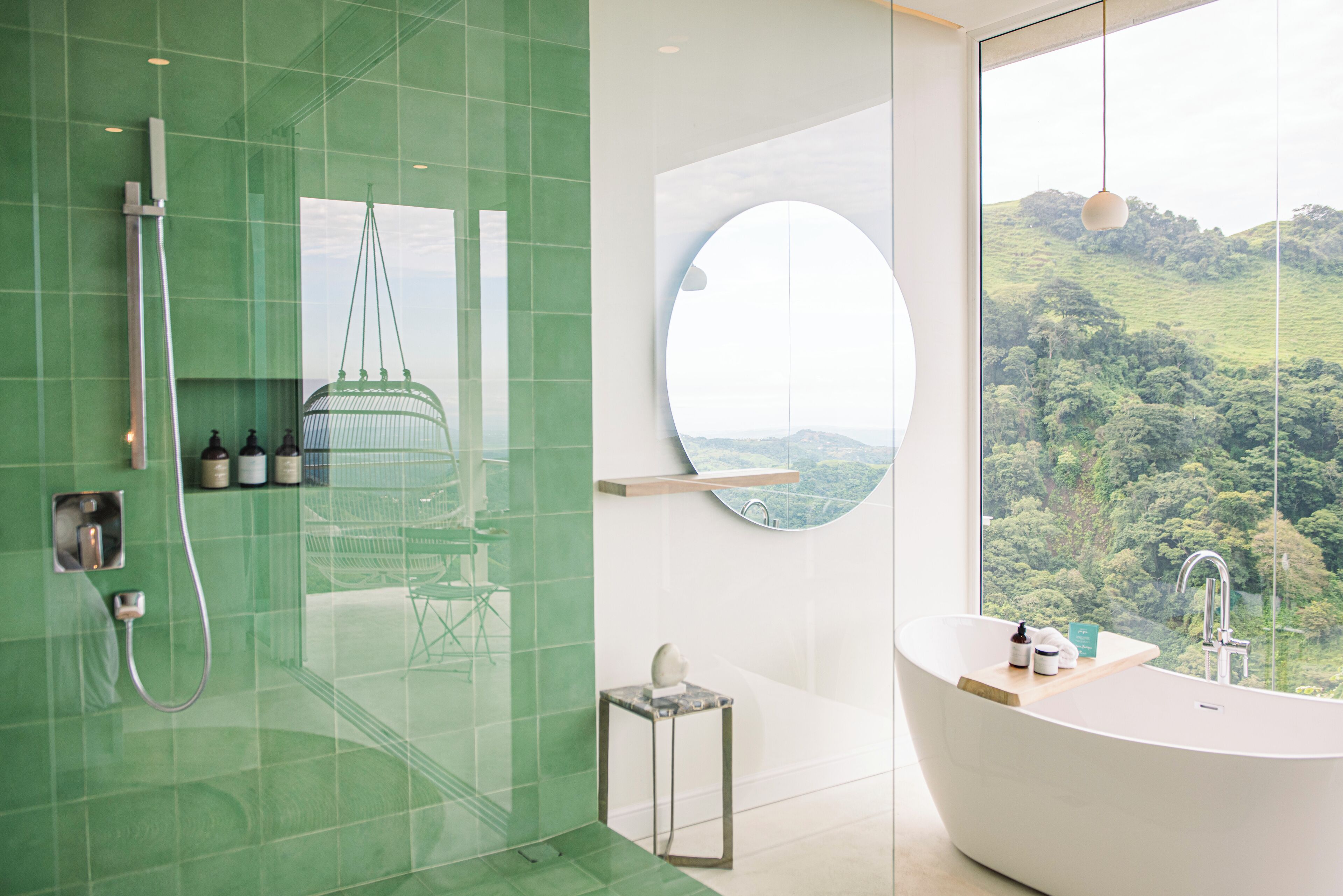 A modern bathroom with a large bathtub, a glass shower enclosure, and a view of a lush landscape.