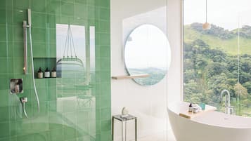 A modern bathroom with a large bathtub, a glass shower enclosure, and a view of a lush landscape.