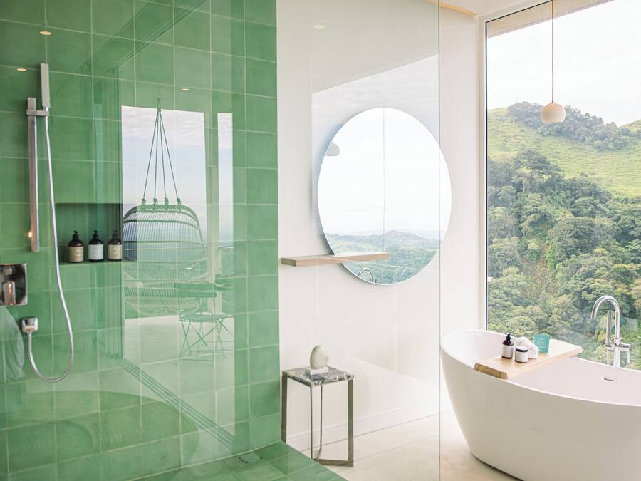 A modern bathroom with a large bathtub, a glass shower enclosure, and a view of a lush landscape.