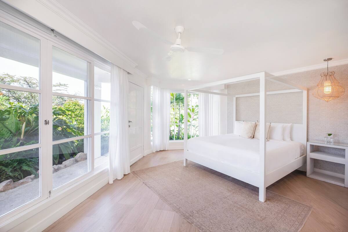 A bedroom with a four-poster bed, large windows, and a ceiling fan.