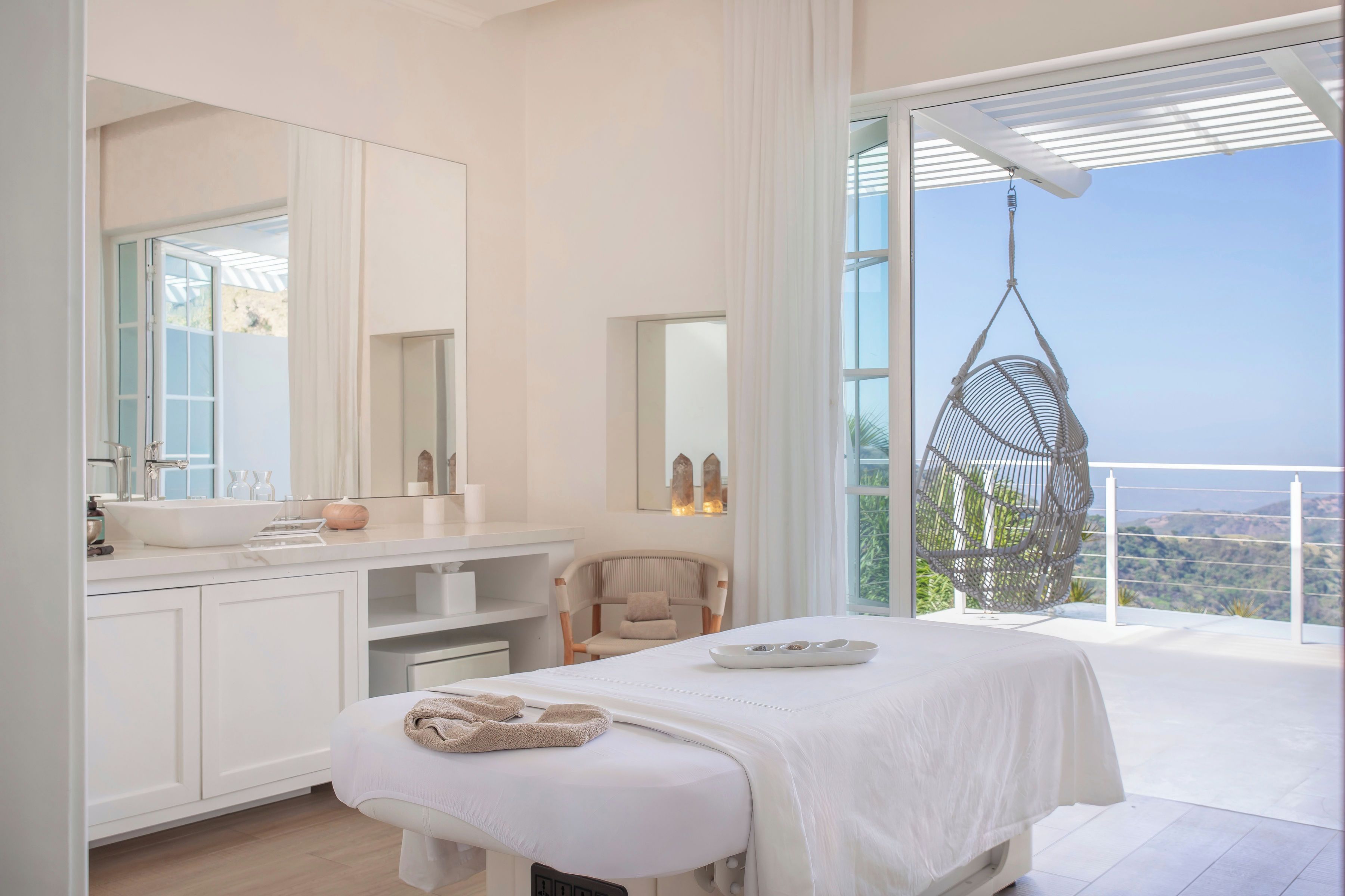 A modern bedroom with a large window, a hanging chair, a bedside table, and a built-in bench.