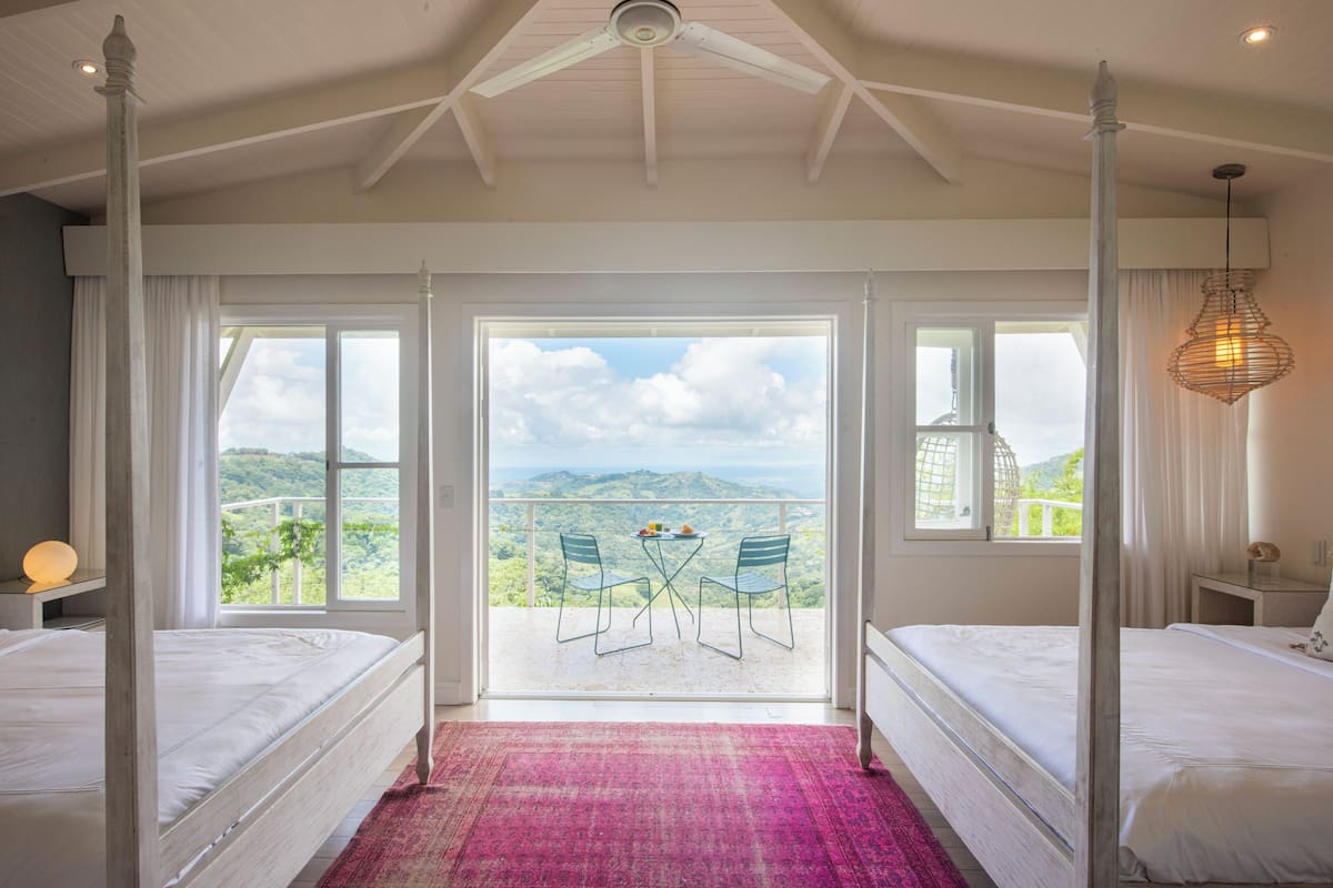 A bedroom with a four-poster bed, a balcony with a table and chairs, and a view of the mountains.