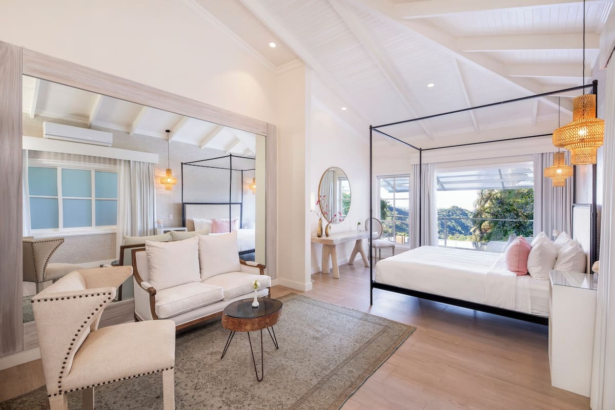 A spacious bedroom with a large bed, a sitting area with a sofa and chairs, and a view of the outdoors.