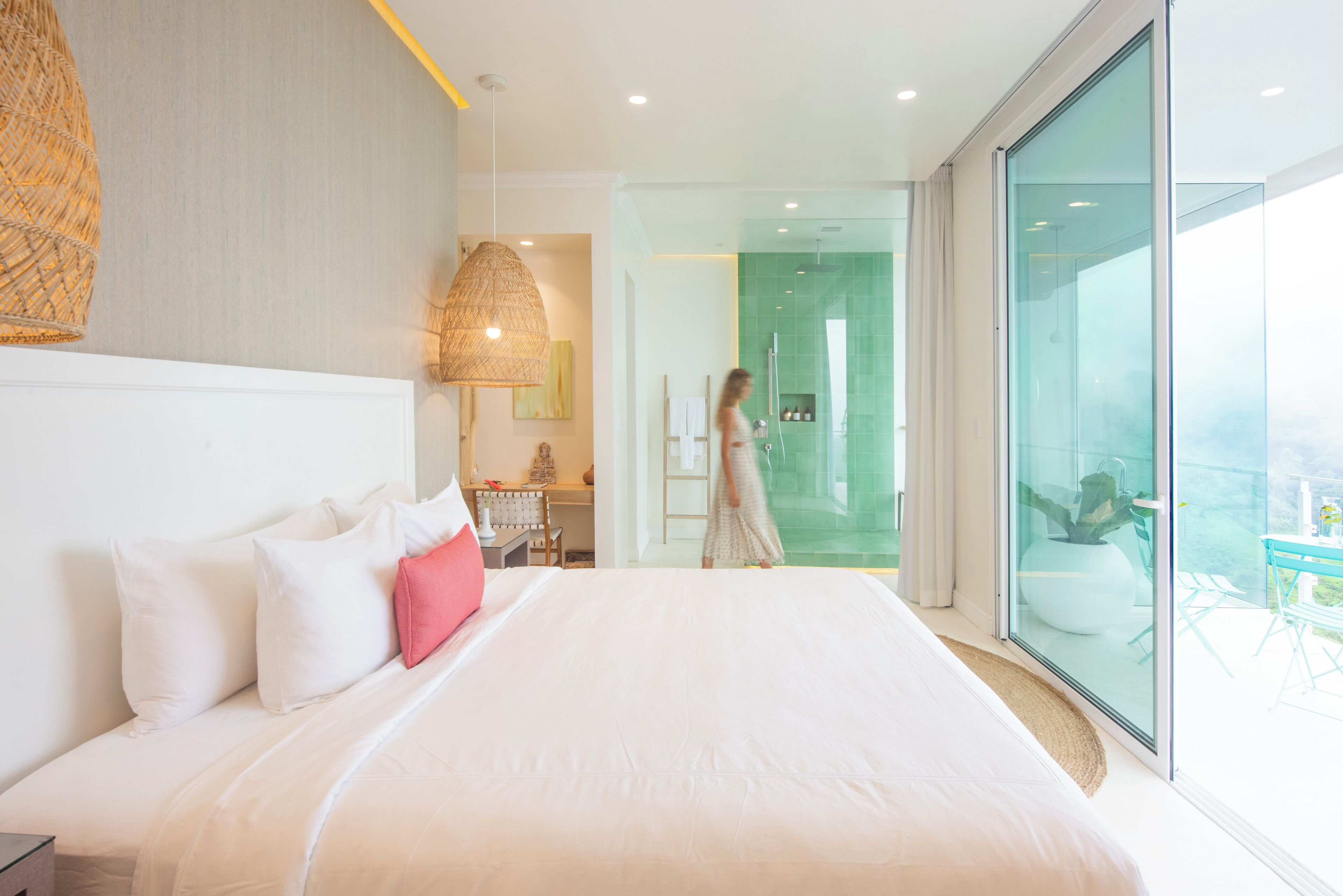 Habitación de hotel moderna con una cama grande, zona de ducha con mampara de vidrio y balcón con mobiliario exterior.